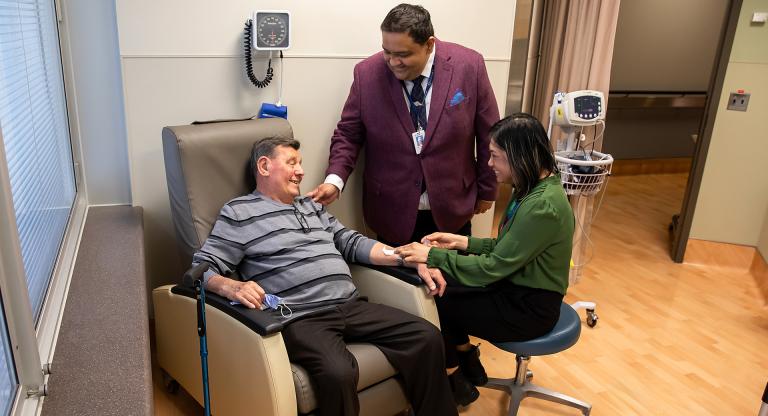 A patient sitting in a chair receiving an infusion with his care team standing beside him.