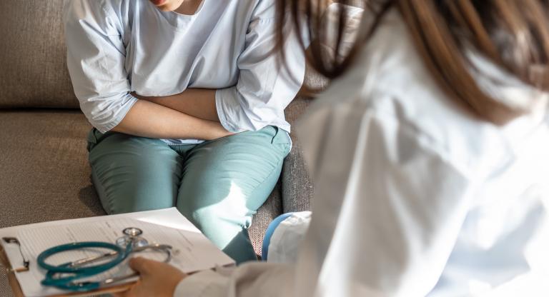 woman sits on couch holding abdomen