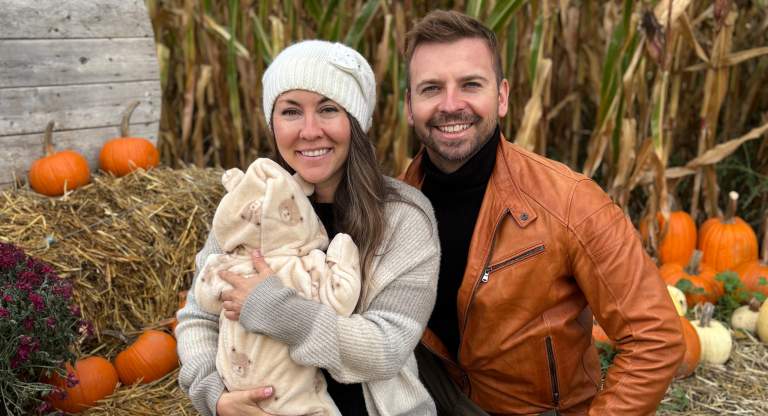 woman holding baby sits next to a man in against a fall backdrop
