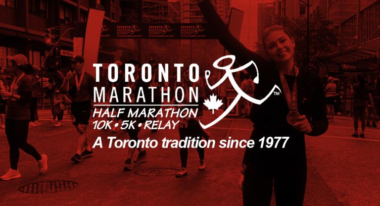 Runners cross a downtown Toronto finish line during the Toronto Marathon, with one participant raising a medal and event branding reading “Toronto Marathon — Half Marathon, 10K, 5K, Relay — A Toronto tradition since 1977.