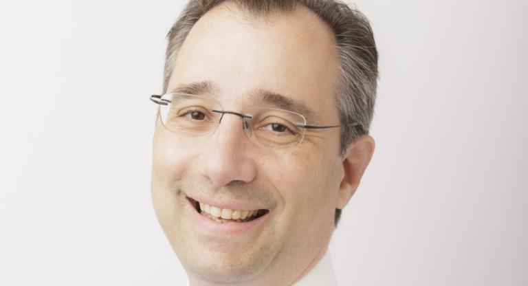 Dr. David Gratzer, head and shoulders portrait. He is looking at the camera smiling and wearing a white shirt with a blue tie
