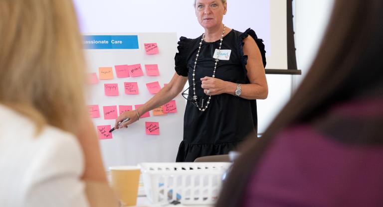 Dr. Lianne Jeffs pointing to a whiteboard with compassionate care descriptors during a presentation. 