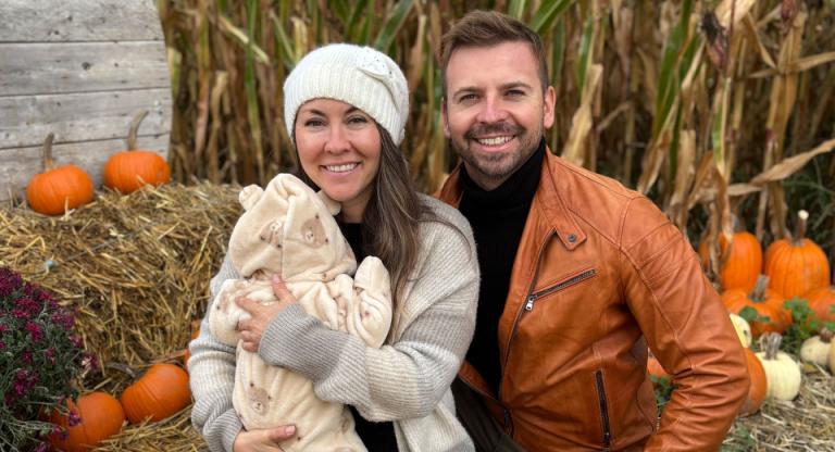 woman holding baby sits next to a man in against a fall backdrop