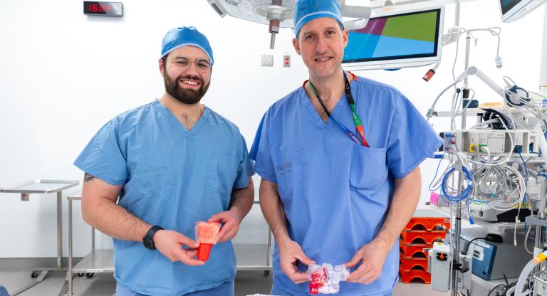 Qwynn  Ferreira and Dr. Joel Davies smiling and standing in an operating room holding the 3D models used in surgery.