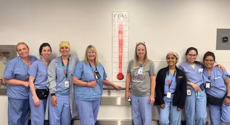 A group of staff members from the Peri-operative services team smile beside a poster showing their recycling goals have been met.
