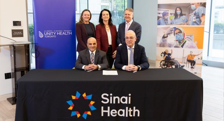 Members of hospital leadership posing in front of Sinai Health and Unity Health Toronto banners.
