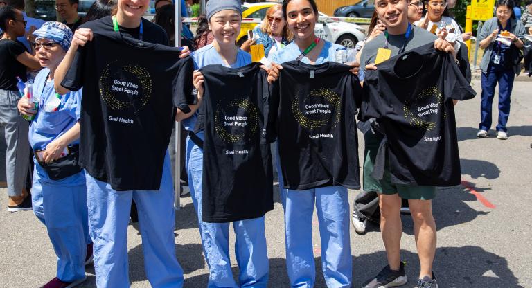 Four Sinai Health employees stand outdoors at the People Appreciation BBQ, smiling and holding black “Good Vibes Great People” T-shirts.