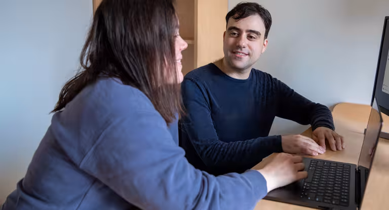 Dr. Michael Wainberg smiling at Isabel Kerrebijn, sitting at a desk beside one another with an open laptop in front of them. 
