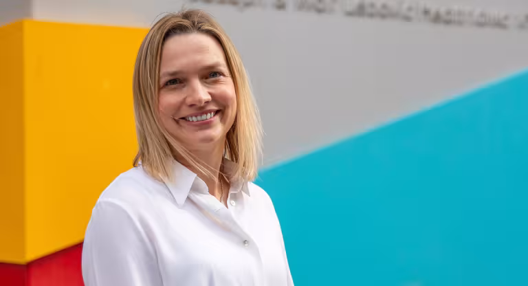 Dr. Jennie Johnstone smiling with a bright background coloured orange, blue and red for the Sinai Health branded colours. 