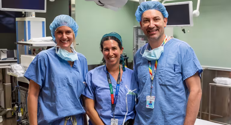 Three people standing in an operating room smiling.