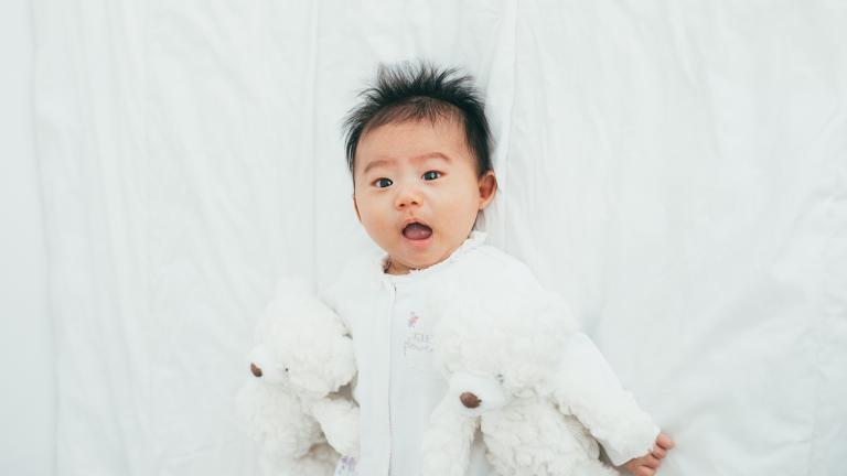 Infant boy wearing a white shirt looking at the camera with white teddy bears on each side of him