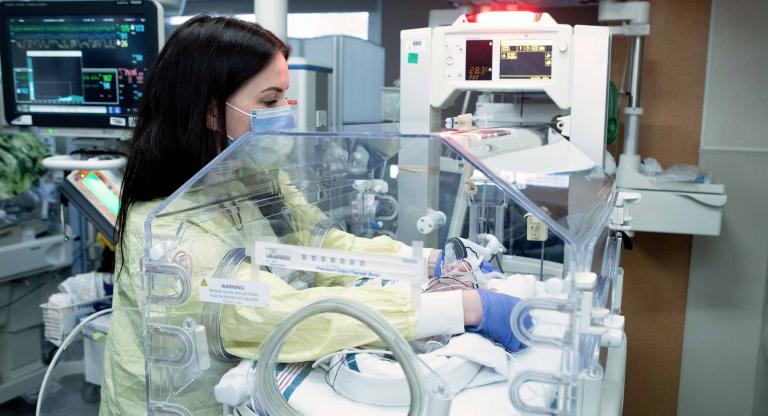 Female nurse with her arms in an incubator with a baby inside