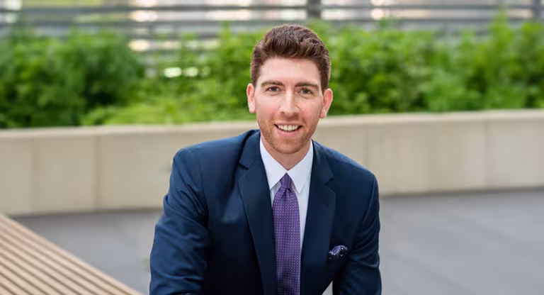 Photo of Jordan Giller on an outdoor patio with shrubs behind him