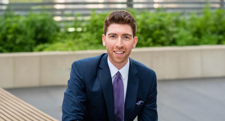 Photo of Jordan Giller on an outdoor patio with shrubs behind him