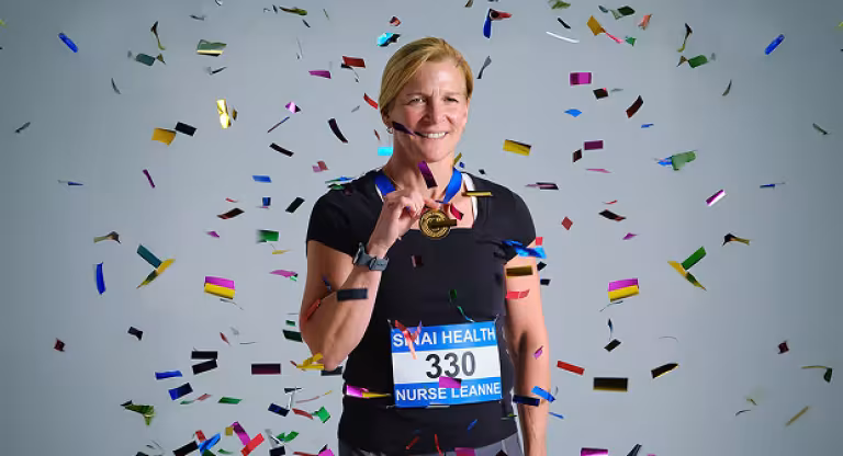 Woman wearing a racing bib and medal stands smiling as confetti falls around her