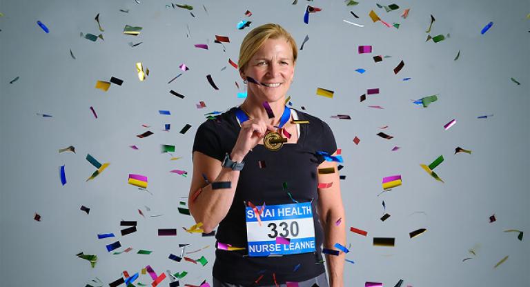 Woman wearing a racing bib and medal stands smiling as confetti falls around her