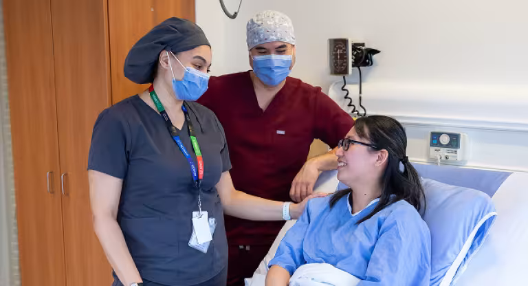 Patient smiles while seated in a hospital bed, interacting with two masked health professionals