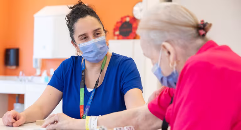 Elderly woman speaks with a masked health professional at a table in a care setting