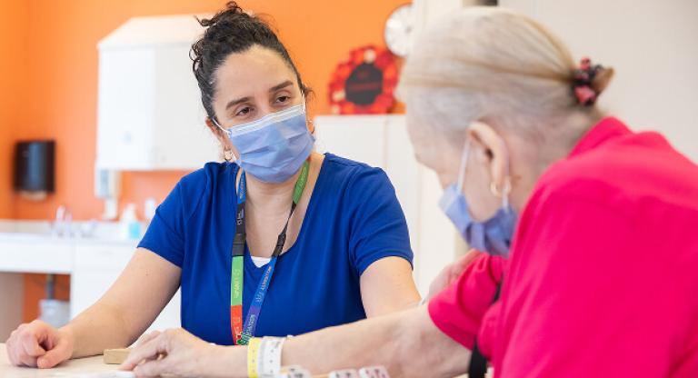 Elderly woman speaks with a masked health professional at a table in a care setting