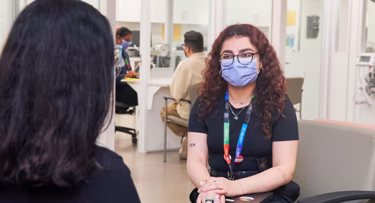 Sinai Health staff member wearing a mask speaks with a colleague in a hospital waiting area.