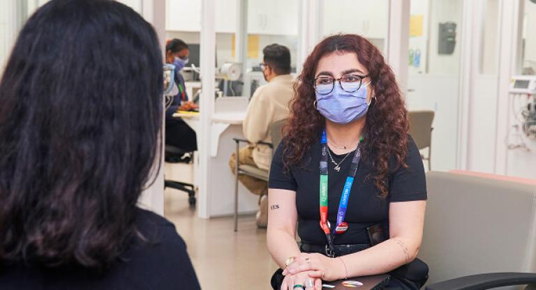 Sinai Health staff member wearing a mask speaks with a colleague in a hospital waiting area.