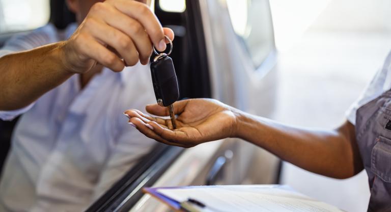 Man in car handing keys to woman holding clipboard