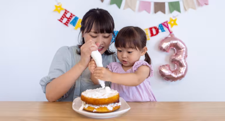 Mother and daughter putting cream on birthday cake at home