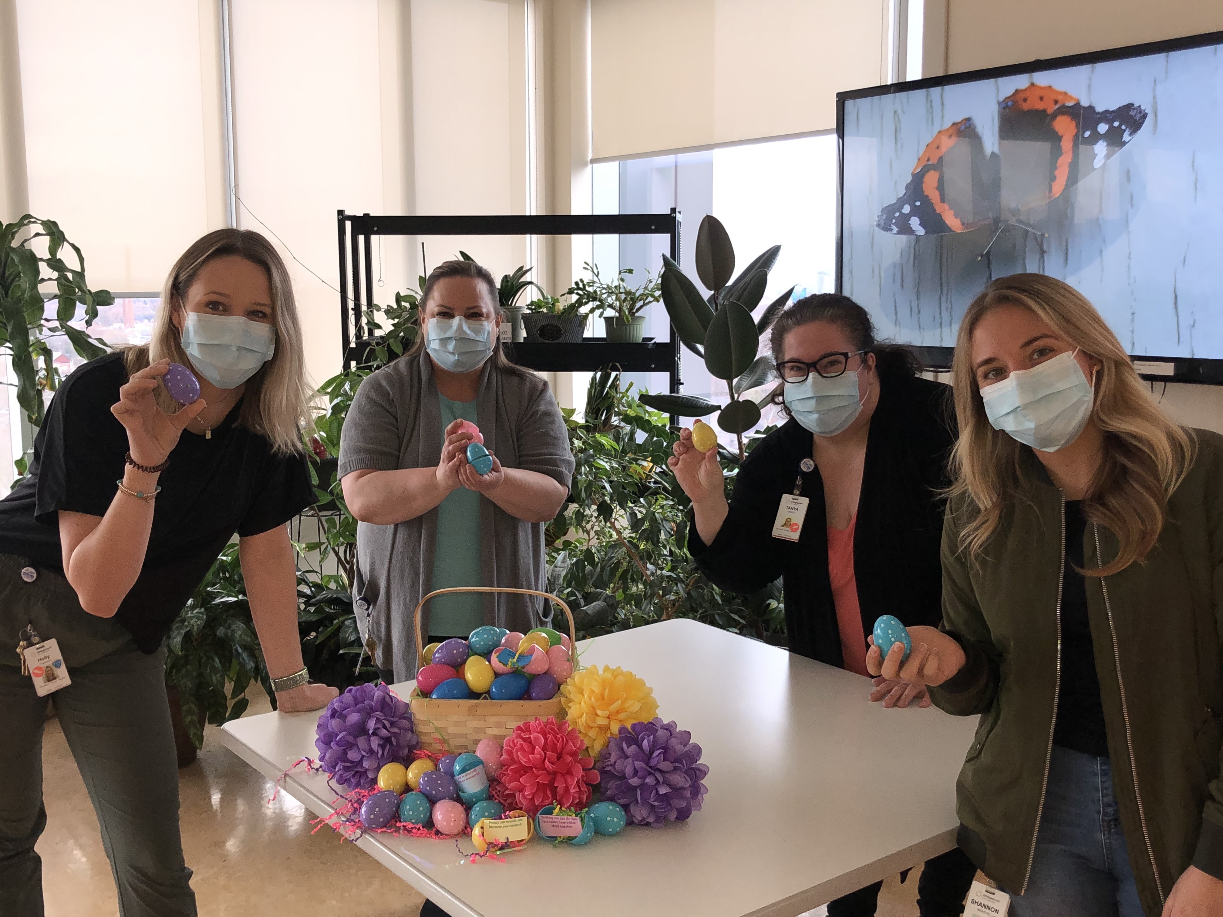 Hospital employees in the patient lounge, standing behind a table with a basket of easter eggs and easter flowers. 