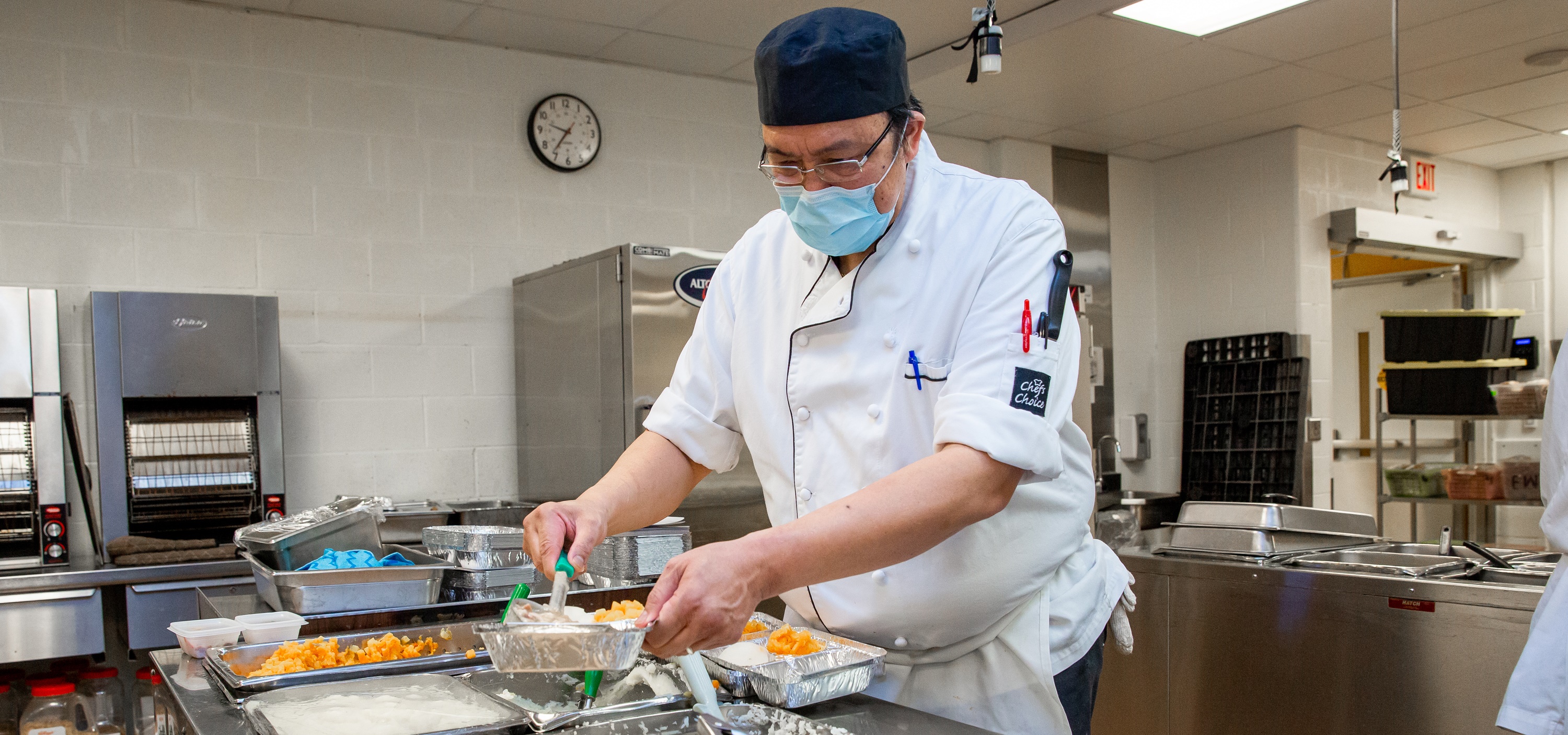 A man in a chef uniform preparing meals in a large industrial kitchen