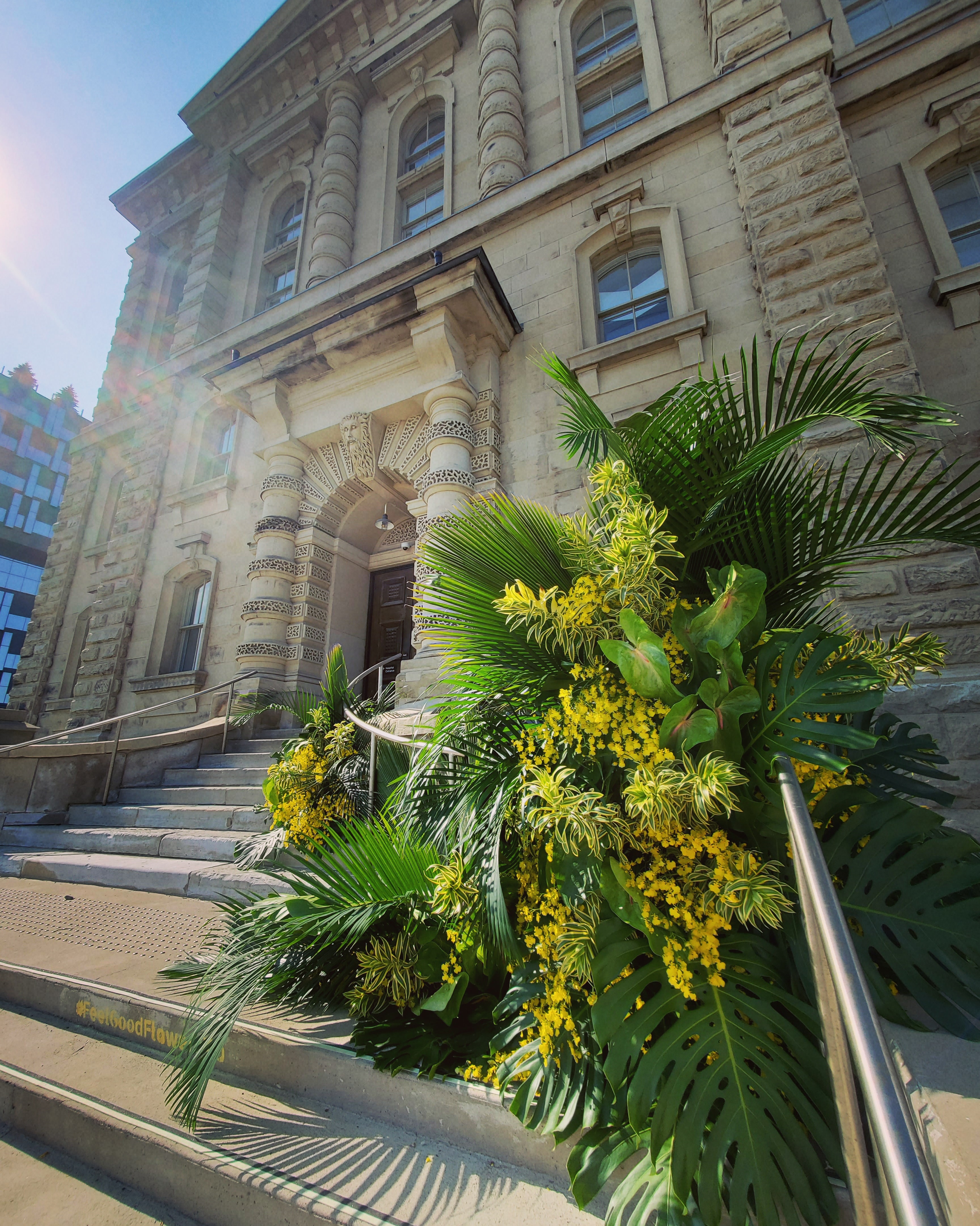 A large green and yellow flower arrangement on some stairs in front of a large old stone building
