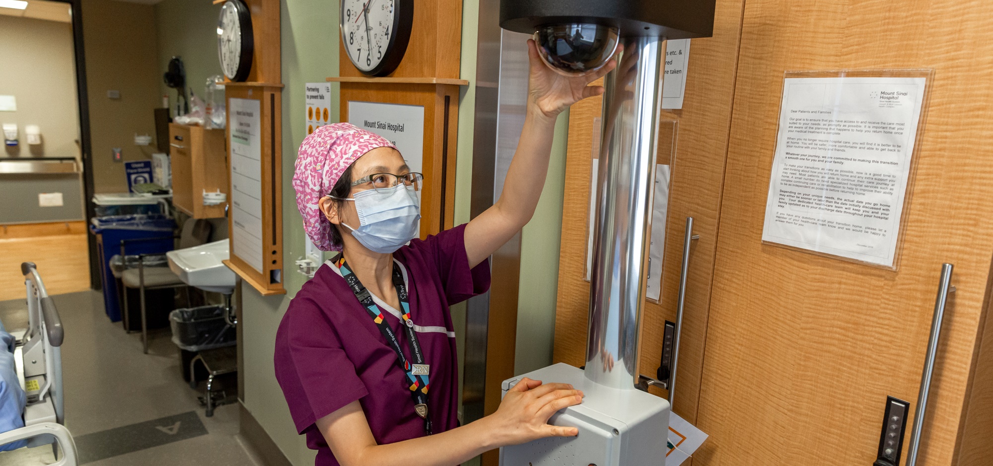 A nurse adjusts a tall mobile camera device in a patient room. 