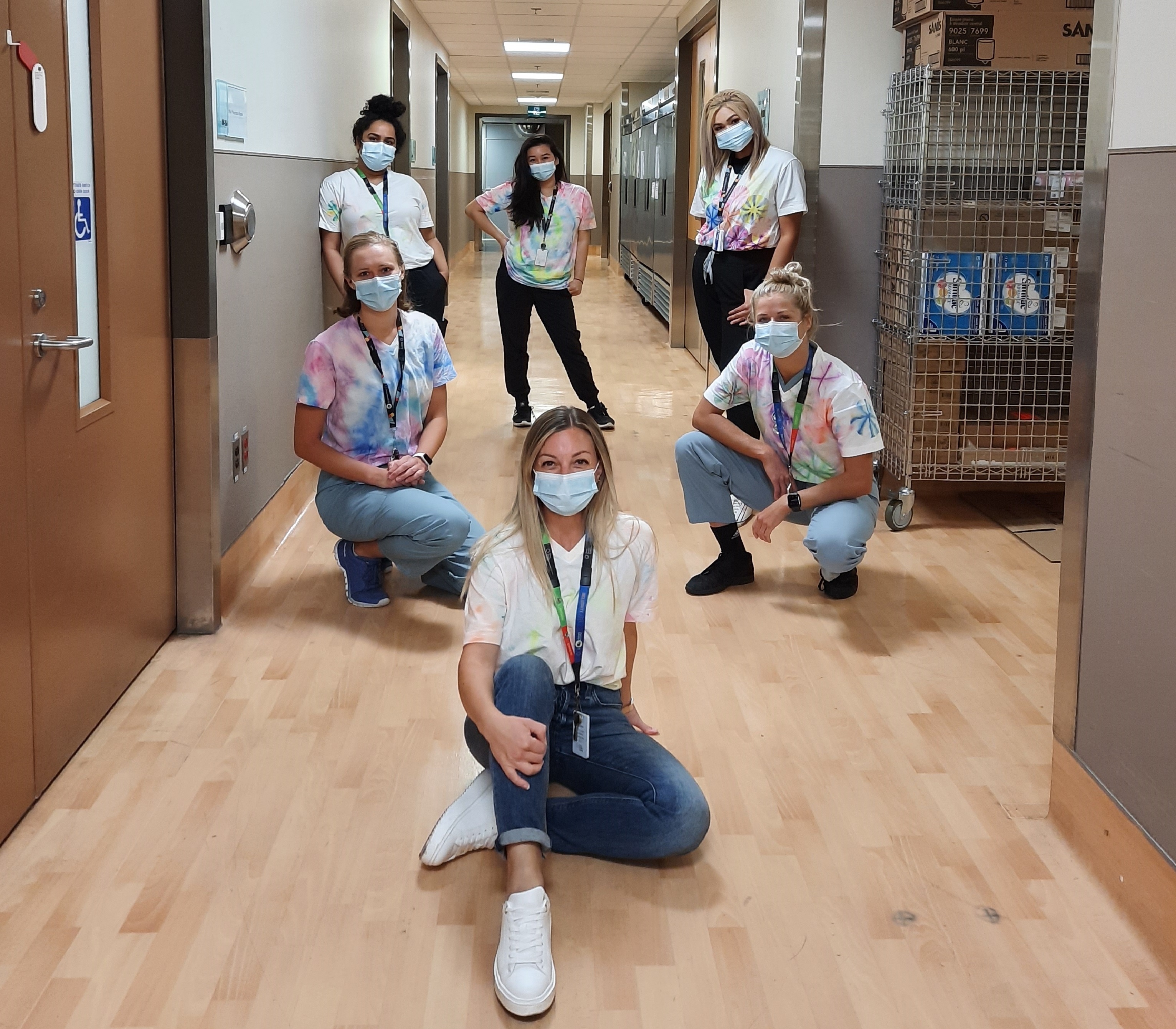 six health care employees in a hospital hallway. They are all wearing tie-dyed shirts and medical masks, looking at the camera