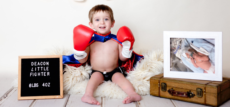 Deacon poses in a cape and boxing gloves next to a picture of himself when he was born