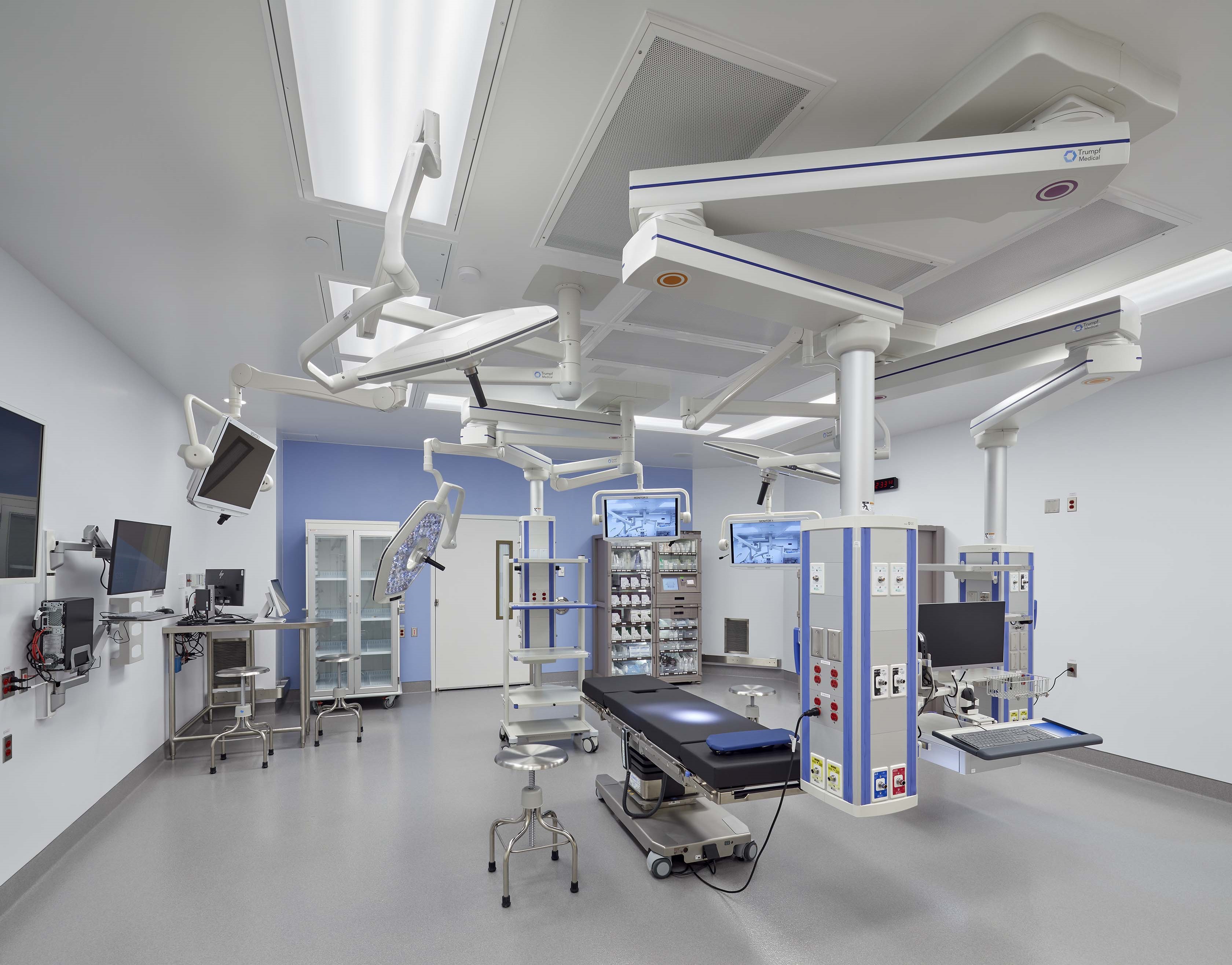 An operating room with equipment including operating table, lights, monitors, computers and equipment cabinets. The room is new and is empty.