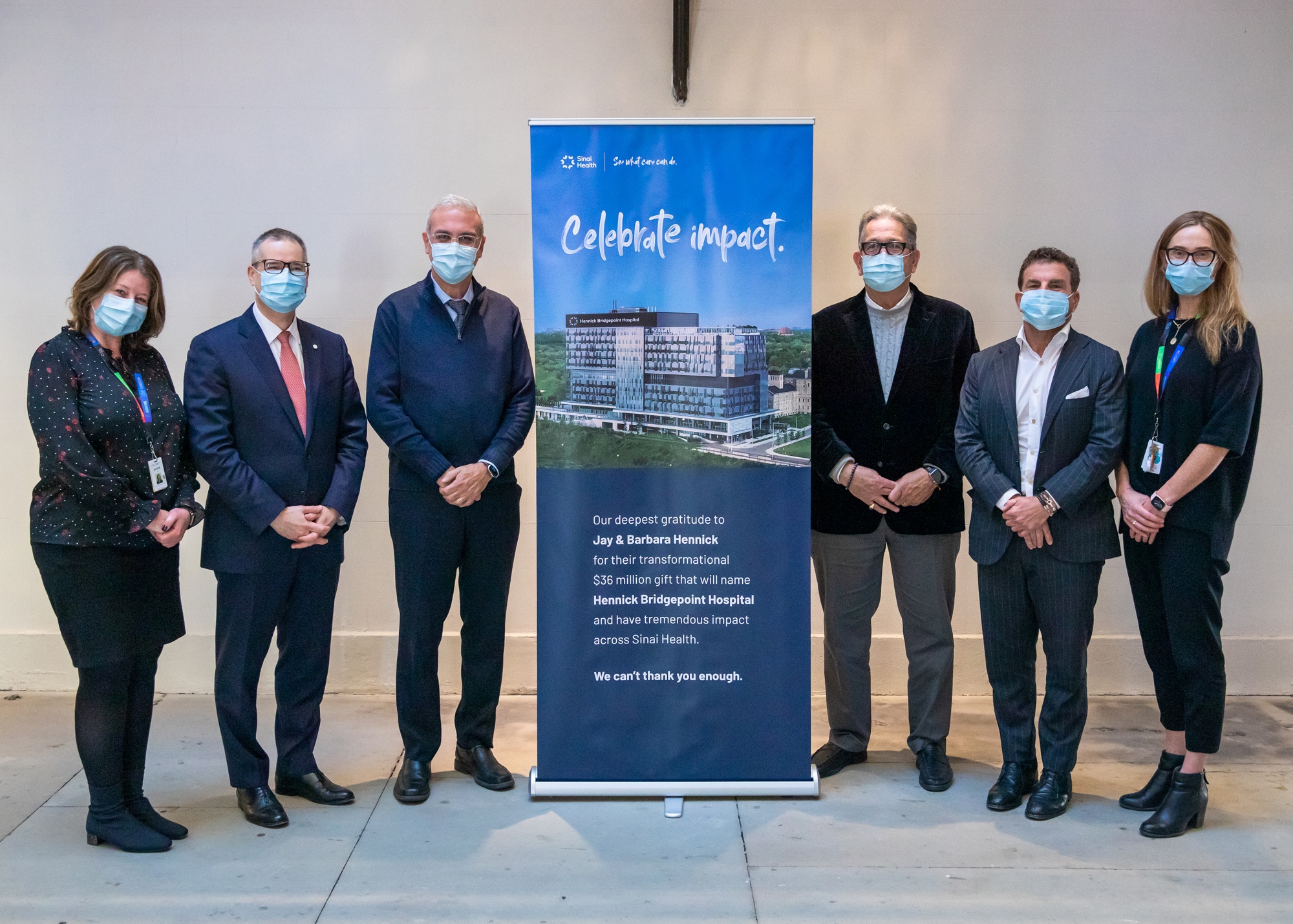 A group of hospital leaders and board members. Three people are standing on either side of a vertical banner that has an image of Hennick Bridgepoint Hospital