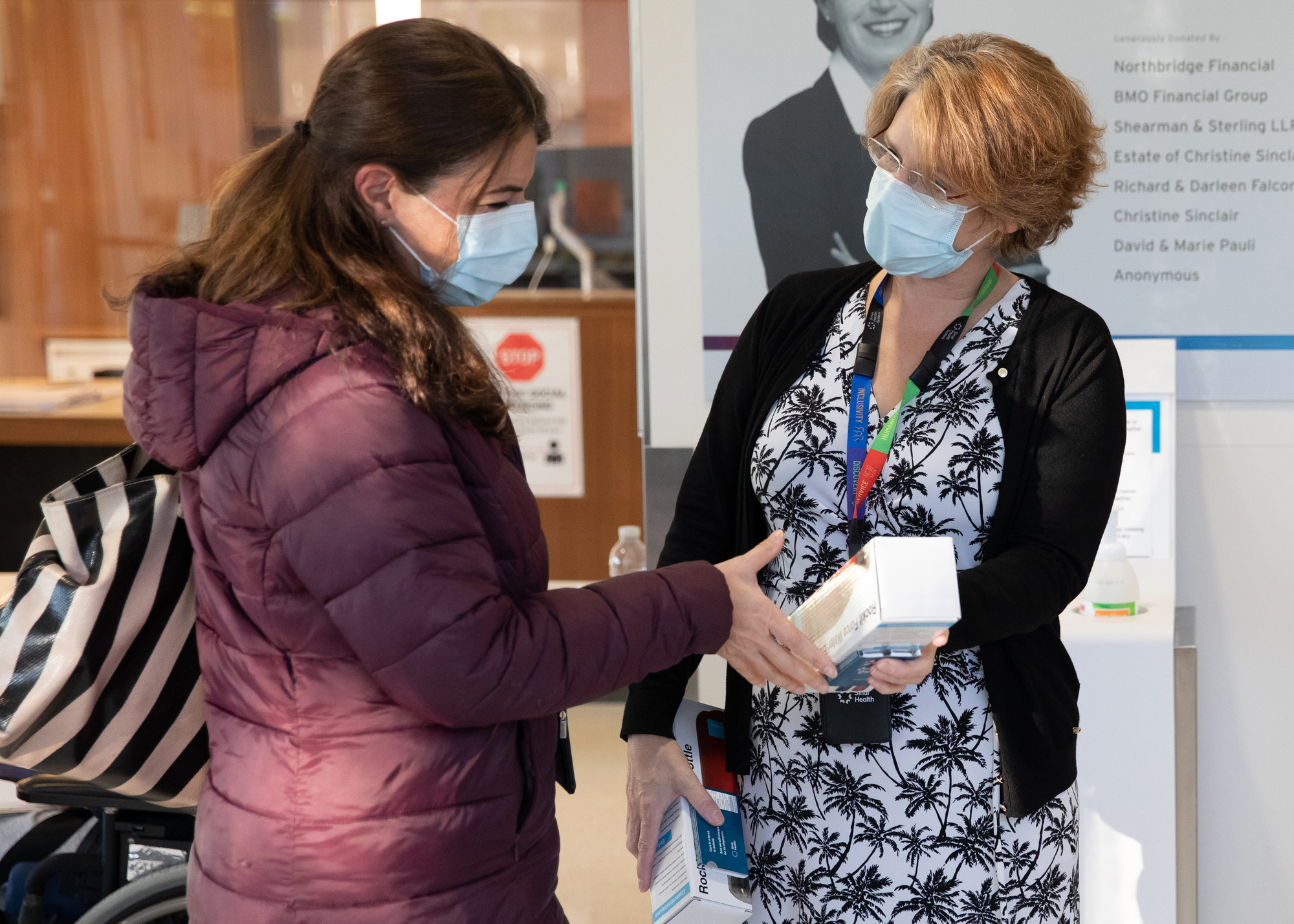 Sinai Health Vice President Kate Wilkinson gives a water bottle to an employee entering the hospital. They are both wearing masks