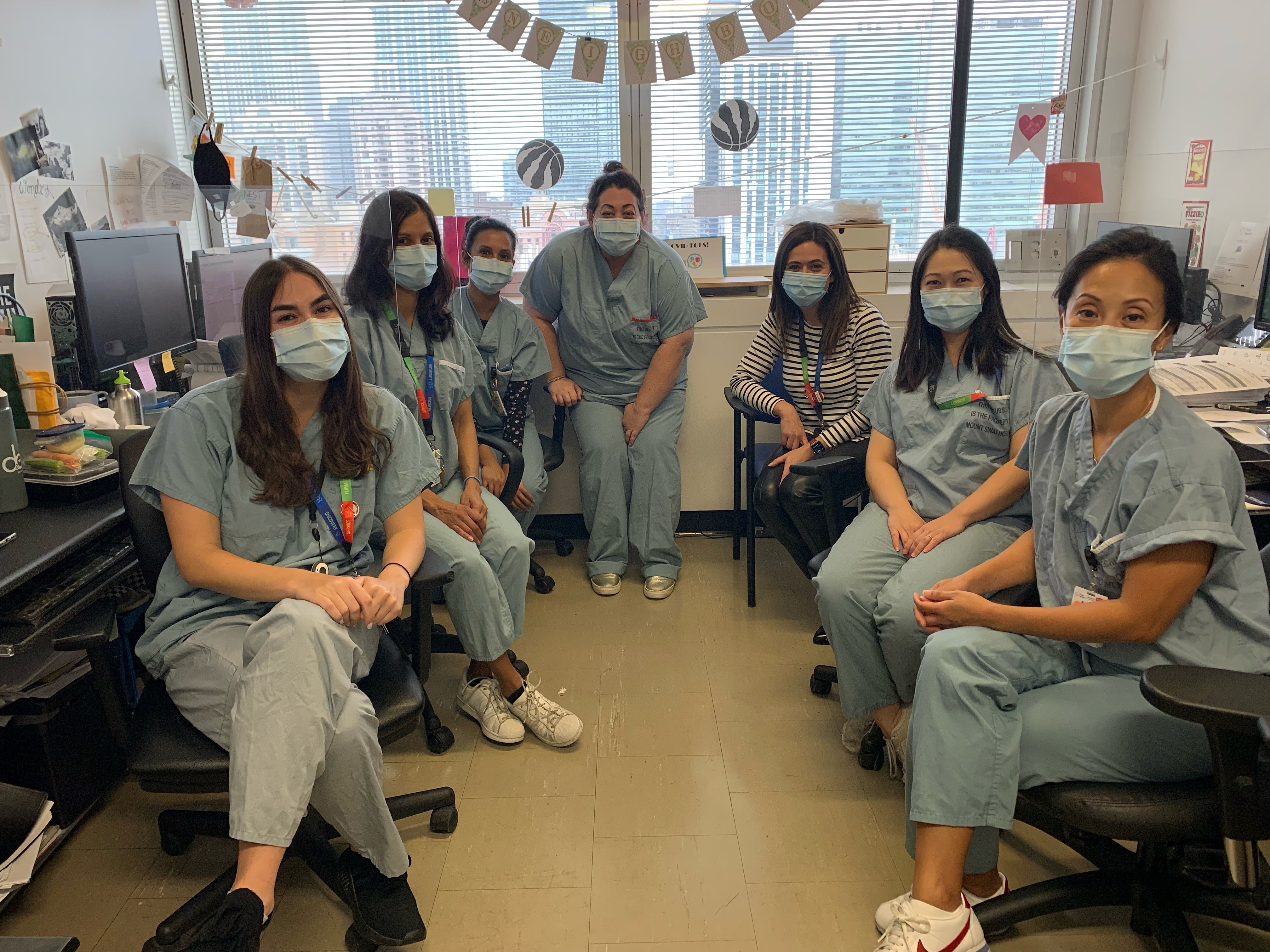 A group of people in an office setting. They are healthcare workers wearing masks and scrubs, seated and looking at the camera