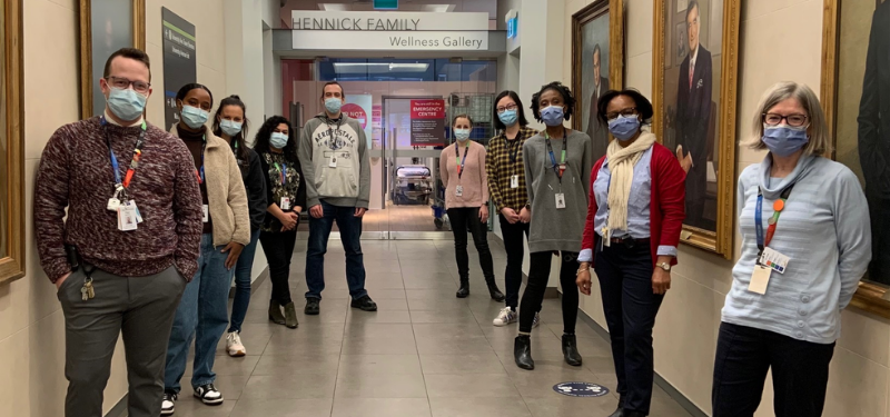 A group of people in a hallway, they are standing in two lines on either side of the hallway and all facing the camera. They are wearing medical masks.