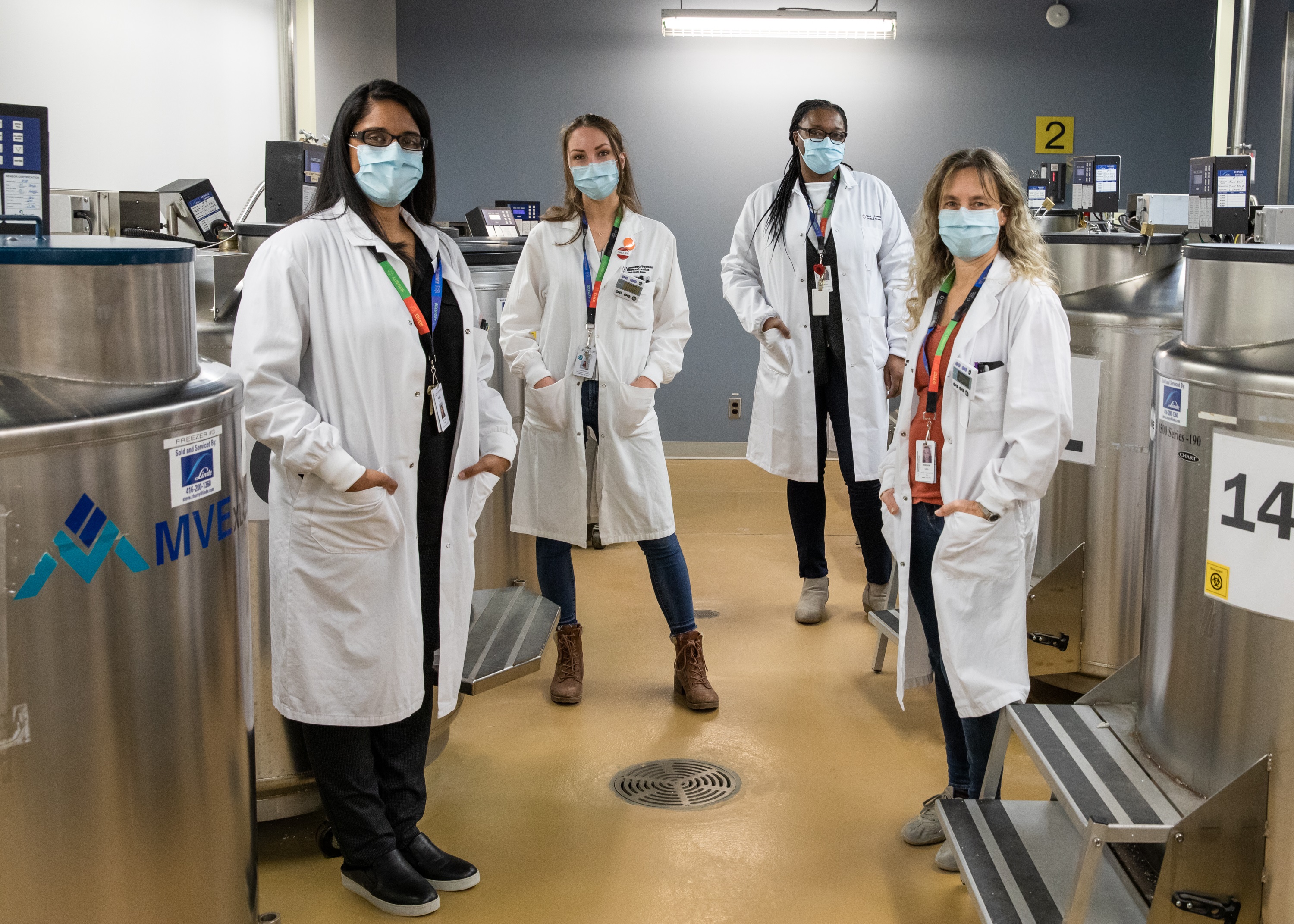A group of women who are laboratory professionals stand in in a room containing large steel vats.